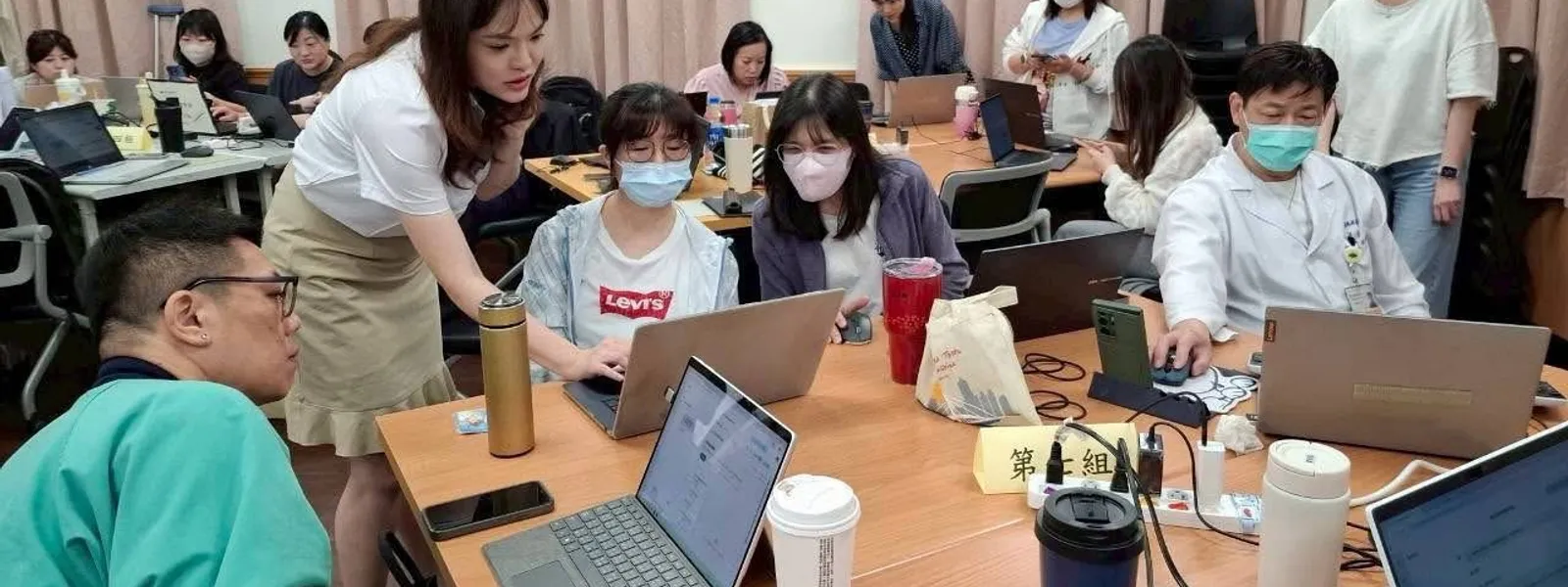 張可佳在企業內訓工作坊現場，俯身指導學員操作筆電